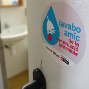 Porta de lavabo oberta, amb el distintiu de la Xarxa de Lavabos Amics de la Menstruació Sostenible